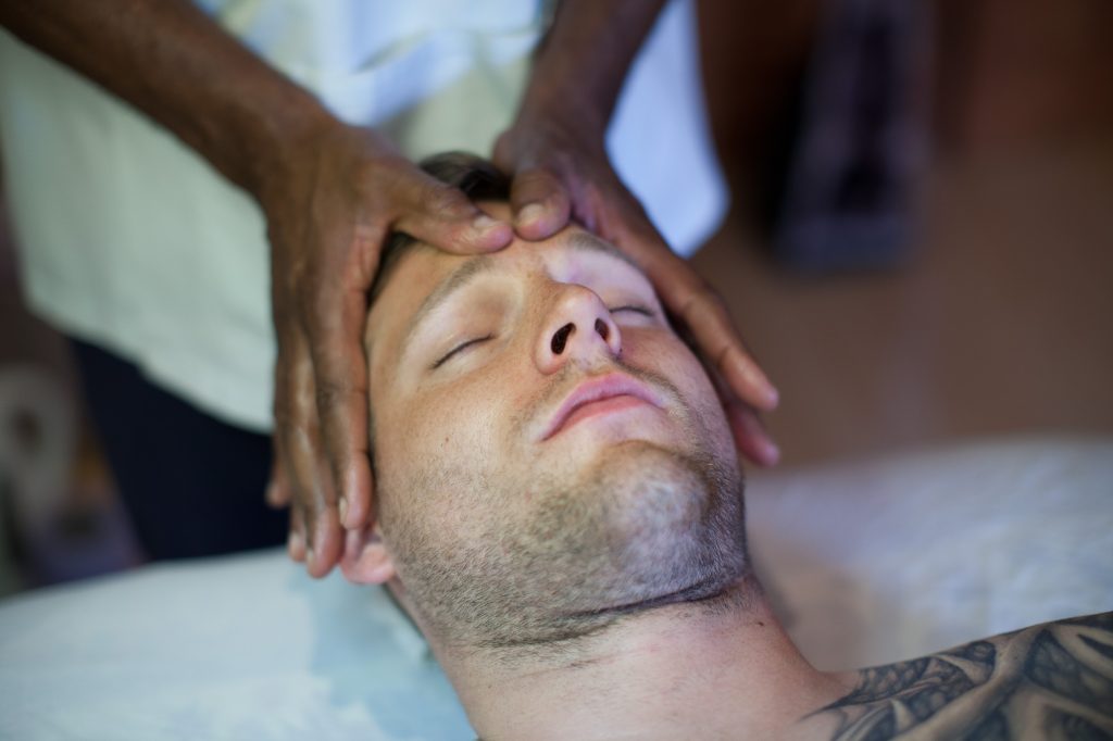 Relaxed man receiving a facial acupressure treatment with pressure applied to his forehead.